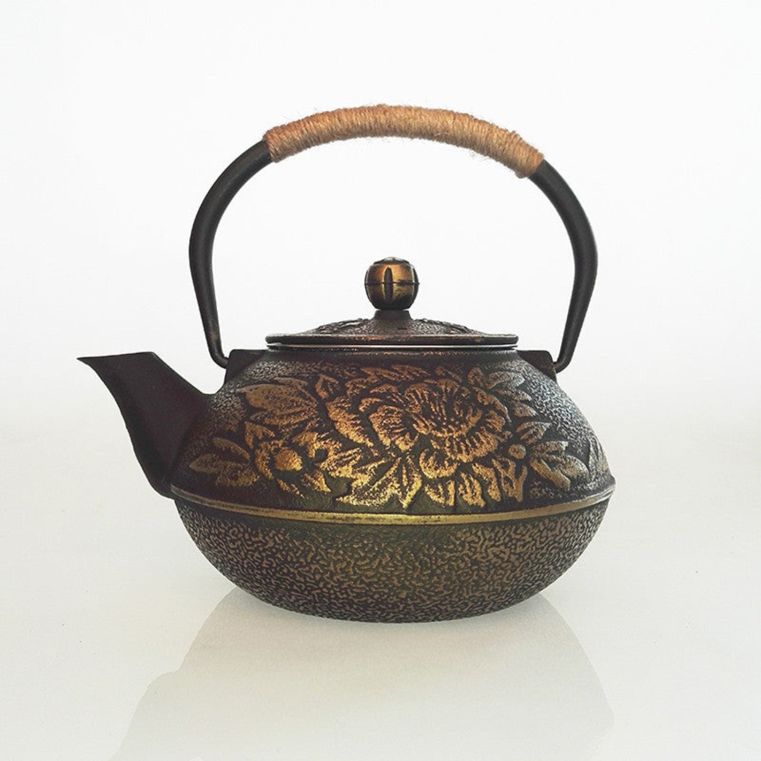 Rose-embossed cast iron teapot with copper or black finish and rattan handle, perfect for brewing tea in a stylish kitchen.
