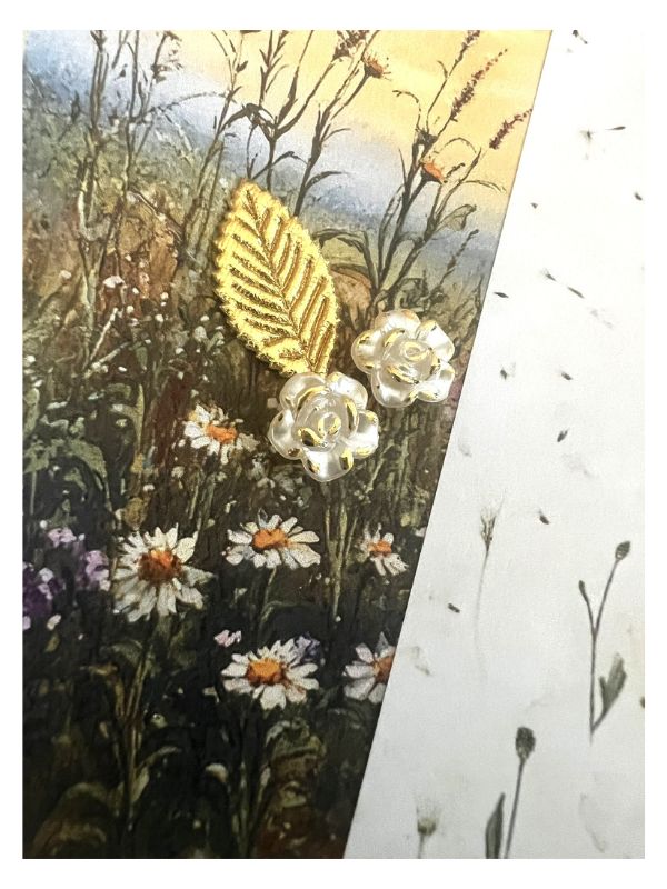 A close-up of a printed or painted floral scene with white daisies, dark stems, and a gold leaf motif, alongside a white textured vertical panel with small black specks.