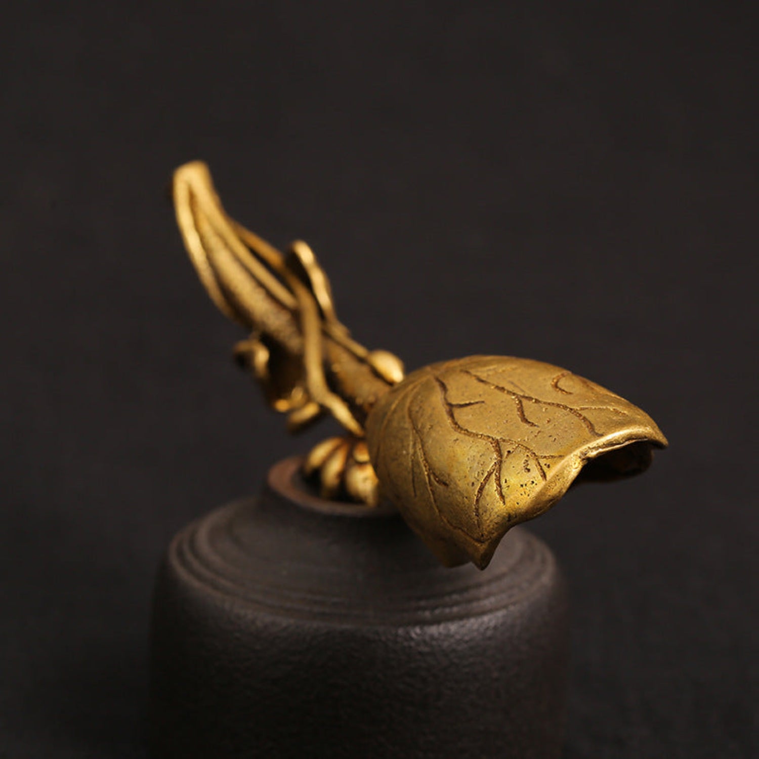 Close-up of a golden brass lotus leaf tea shovel, artisan scoop for tea, with detailed leaf design and polished finish.