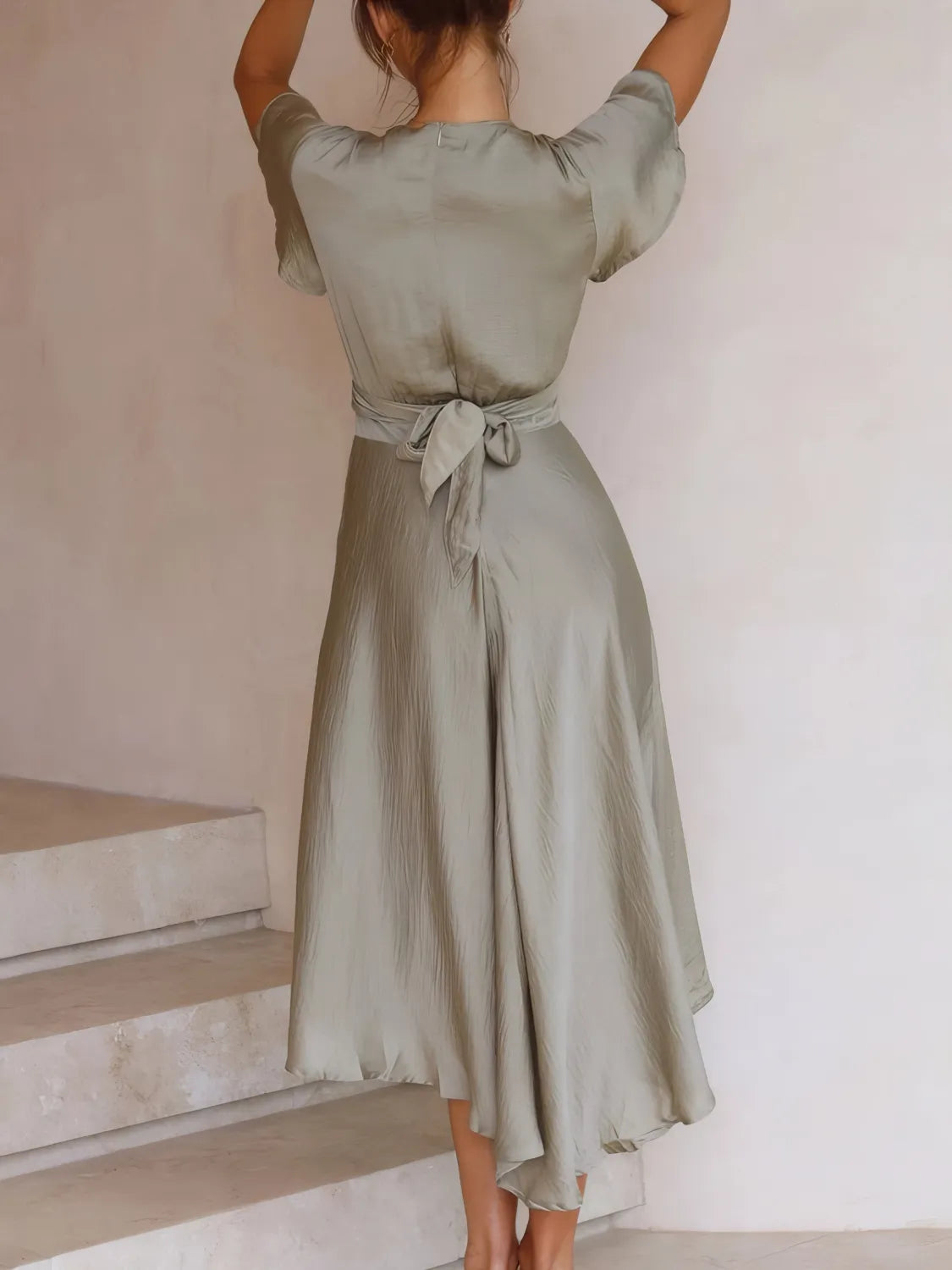 Sage green Flutter Skies high-low dress with plunge neckline and crisscross back, worn by a model showcasing its stylish design.