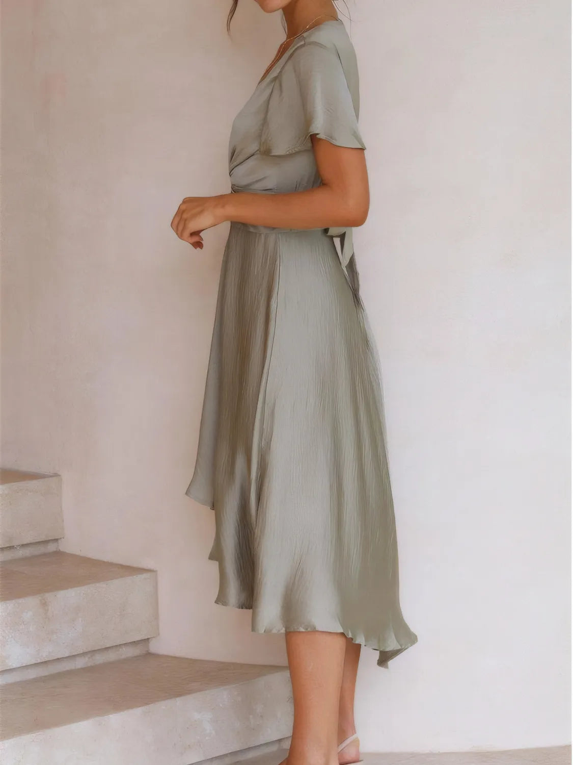 Sage green Flutter Skies high-low dress by Trendsi, featuring a plunge neckline and crisscross back, styled on a side-view model.